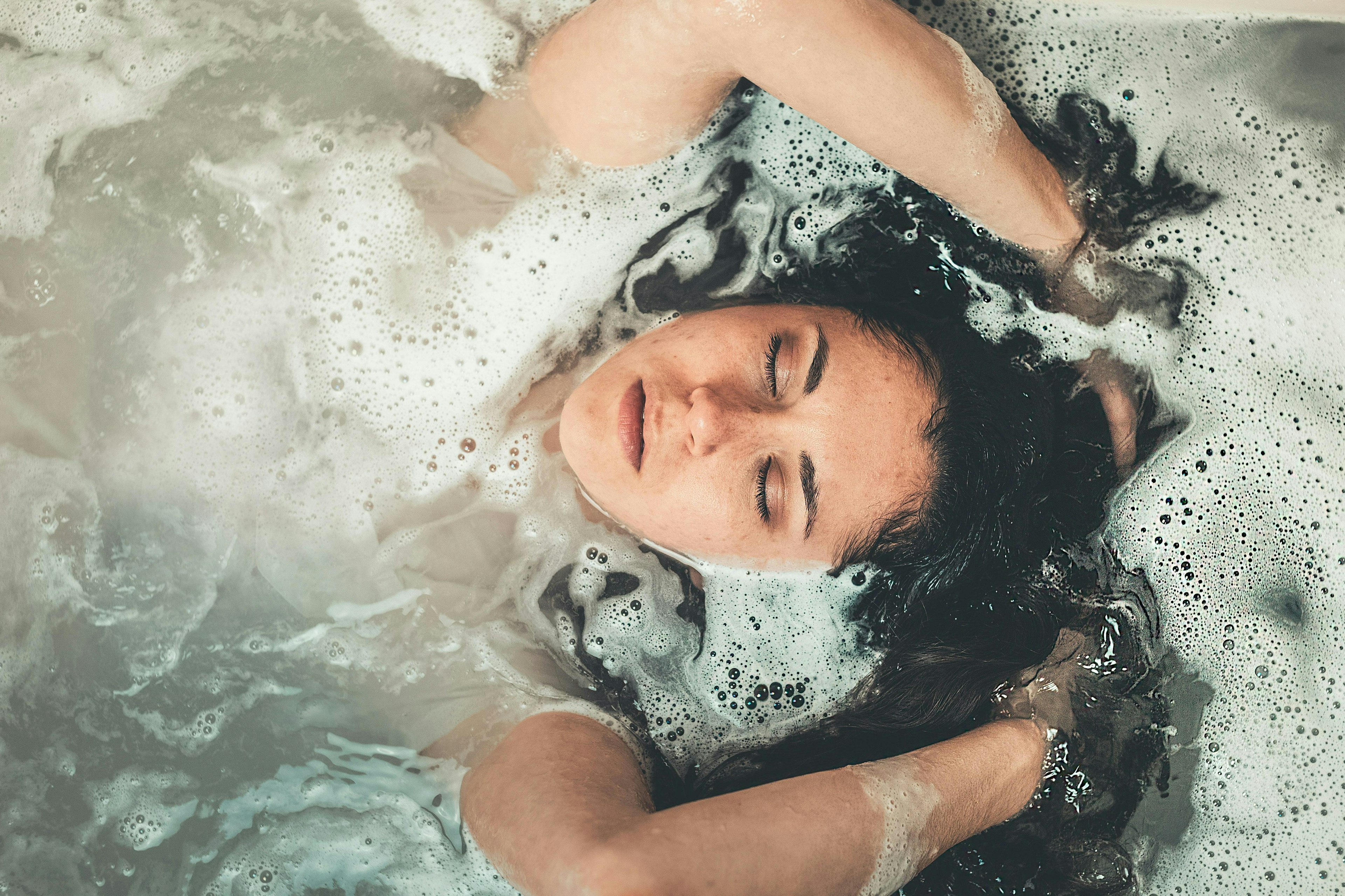 Femme vue de haut prenant un bain les cheveux libres et de la mousse à la surface de l'eau